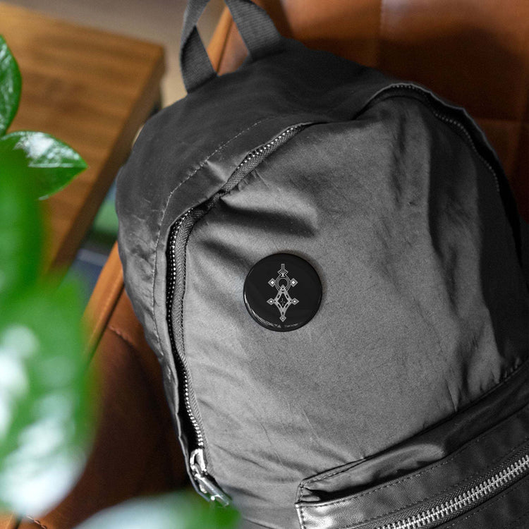 Black round pin with geometric design on black backpack, steel shell with glossy mylar cover, magnetic backing, scratch-resistant finish