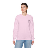 Woman wearing light pink Heavy Blend™ Crewneck Sweatshirt with small chest embroidery, paired with blue jeans