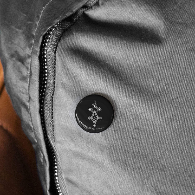 Round pin with black and white design, steel inner shell, and magnetic backing on gray fabric with zipper.