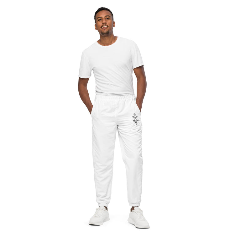 Man wearing white men track pants with elastic ankle cuffs and white sneakers standing against white background
