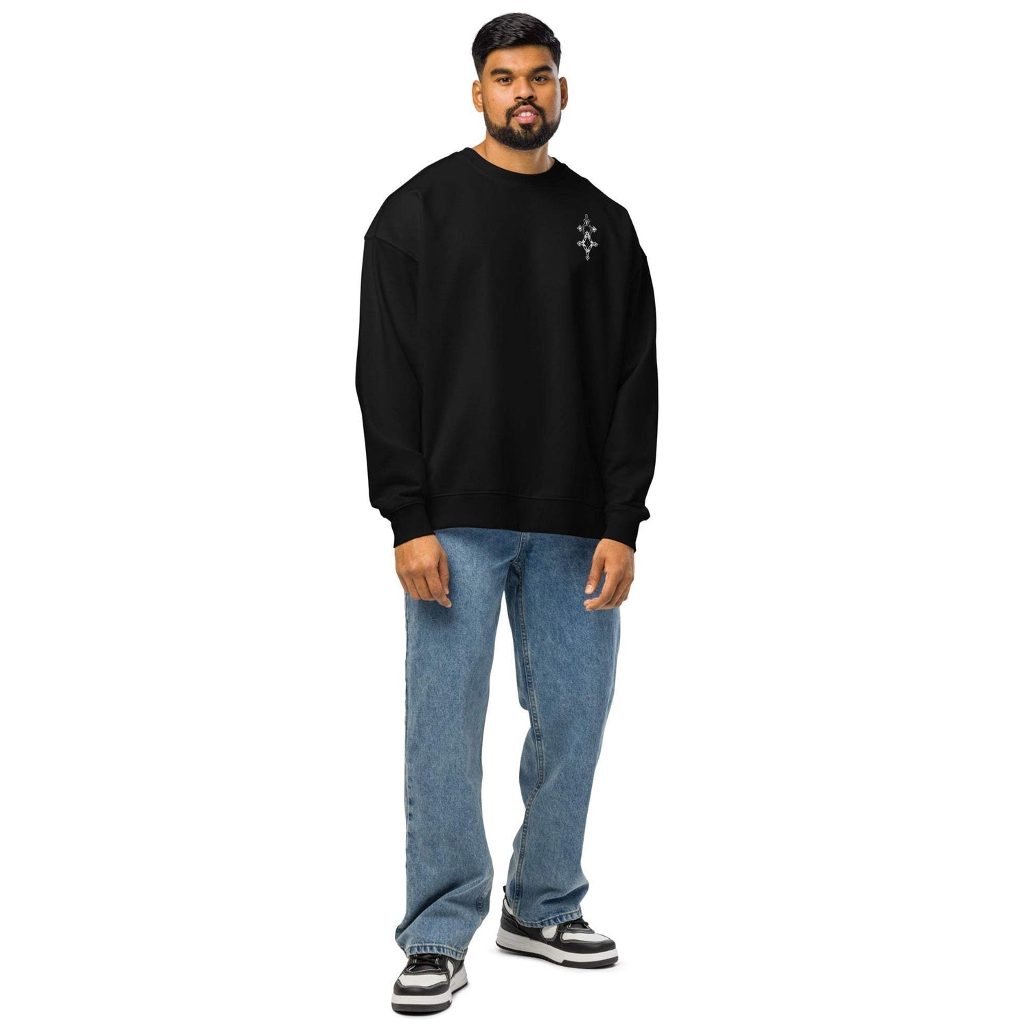 man wearing black organic oversized sweatshirt with jeans and sneakers standing against white background