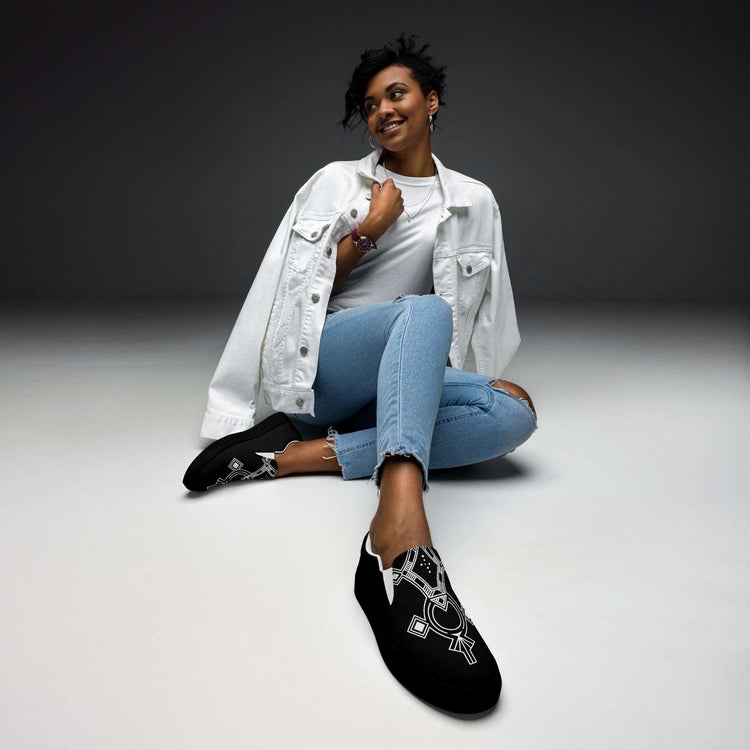Woman wearing black women’s slip-on canvas shoes with white geometric pattern sitting on the floor in casual outfit