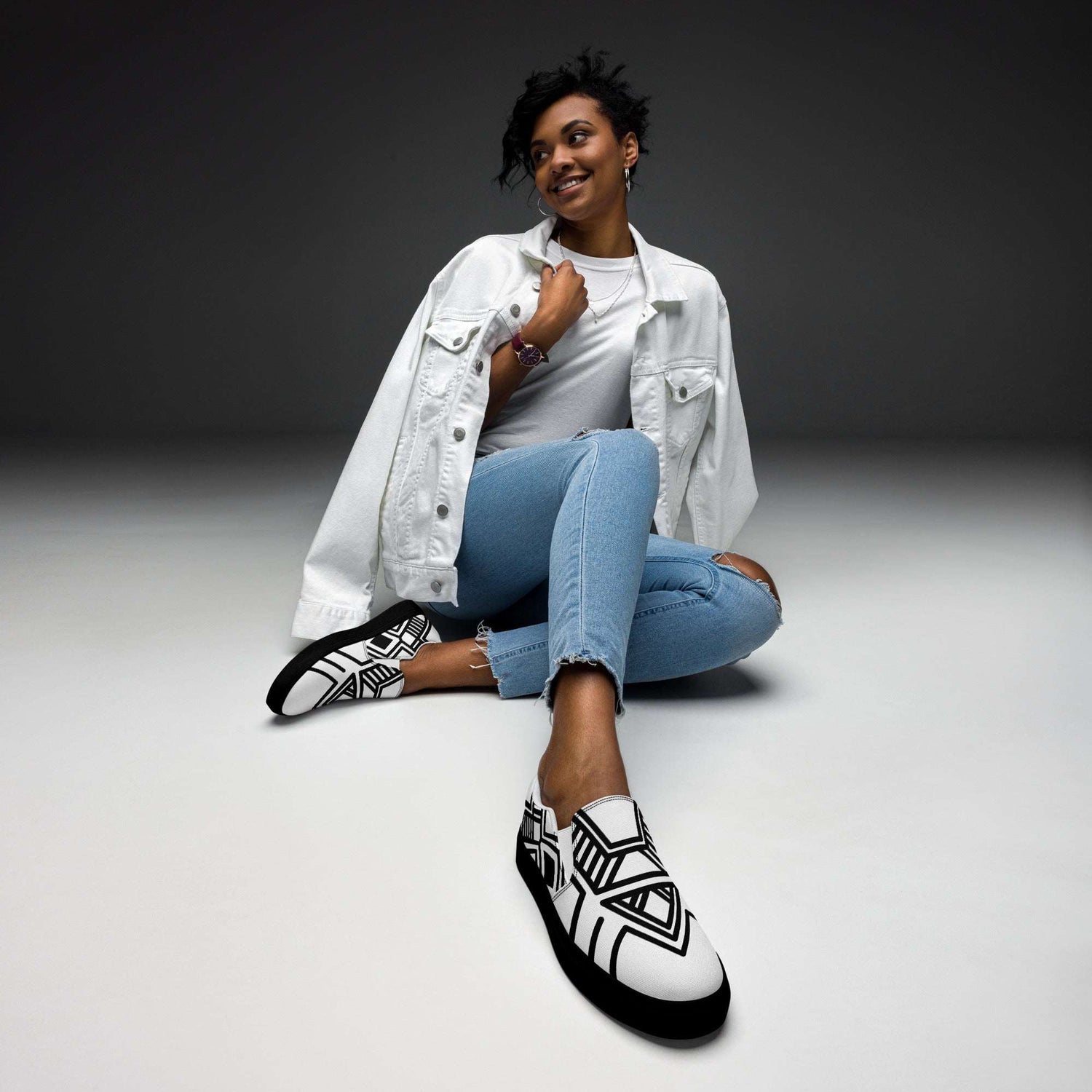 Woman wearing stylish black and white women’s slip-on canvas shoes with geometric pattern sitting on the floor in casual outfit