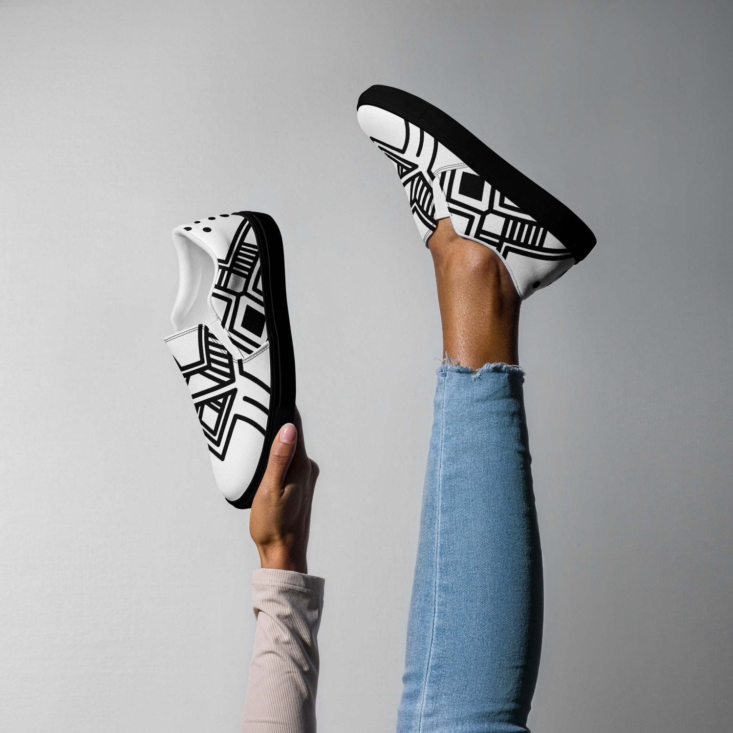 Black and white geometric patterned women’s slip-on canvas shoes with rubber soles, worn with blue jeans.