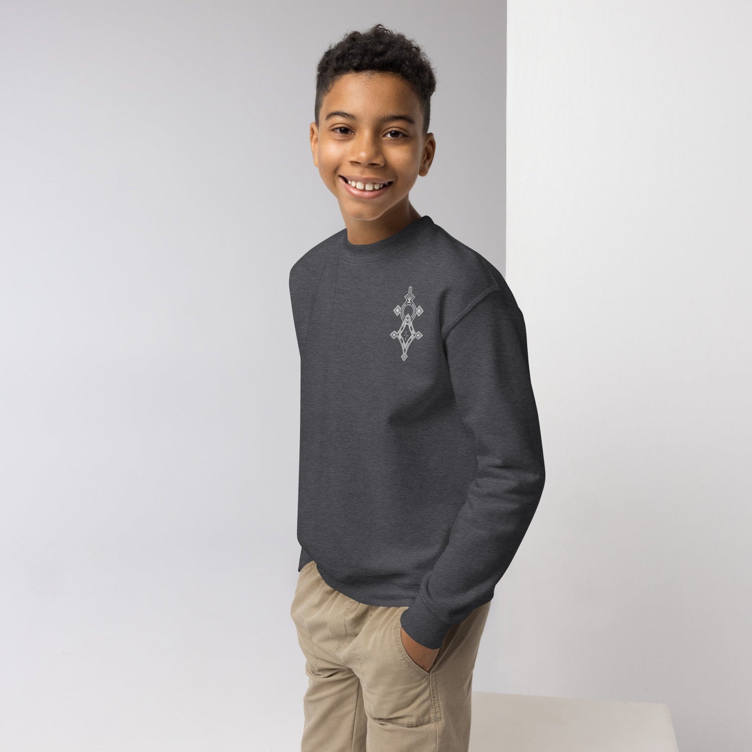 Boy wearing dark gray youth crewneck sweatshirt with graphic design and beige pants smiling