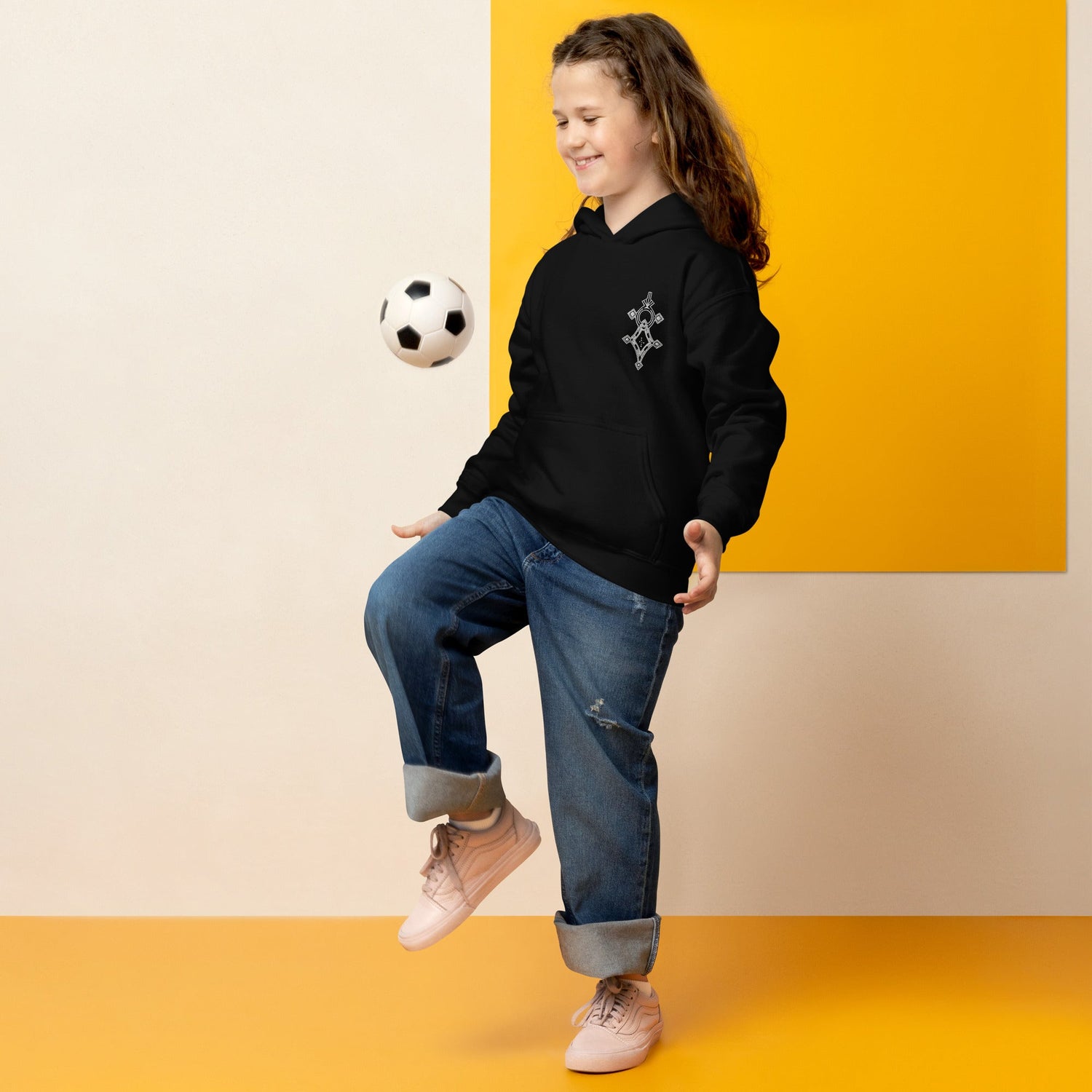 Child wearing black youth heavy blend hoodie playing with soccer ball against yellow background