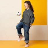Child wearing a charcoal youth heavy blend hoodie playing with a soccer ball against a yellow background