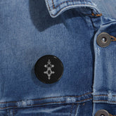 Round pin with black glossy finish and geometric design on denim jacket
