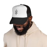 Black and white trucker cap with mesh back and adjustable snap closure worn by a smiling man