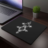 Rectangular black mouse pad with white geometric design on wooden desk next to laptop and small plant