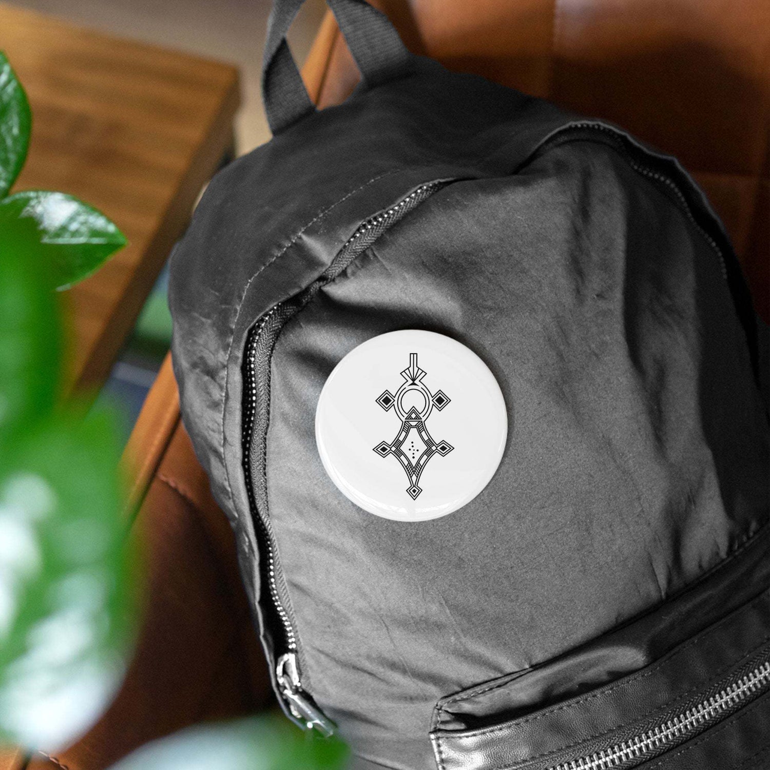 Round pin with a geometric design attached to a black backpack, featuring steel shell and glossy mylar cover.