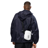 Man wearing white utility crossbody bag with adjustable strap over navy jacket, showing back view