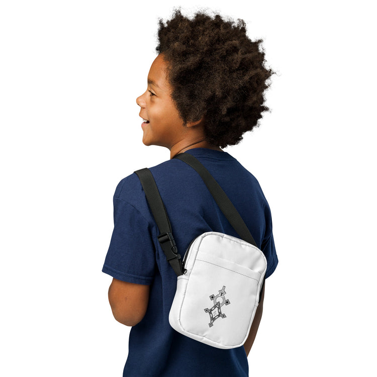 White utility crossbody bag with adjustable black strap worn by a person in a navy shirt, featuring two zippered pockets and a small printed design on the front.