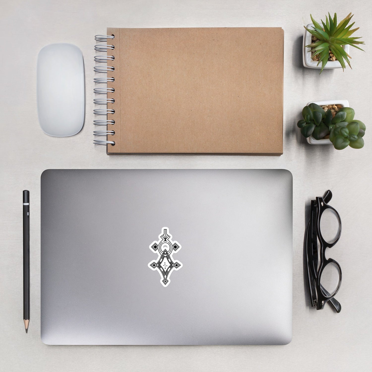 Bubble-free sticker on laptop with notebook, mouse, pencil, glasses, and plants on desk