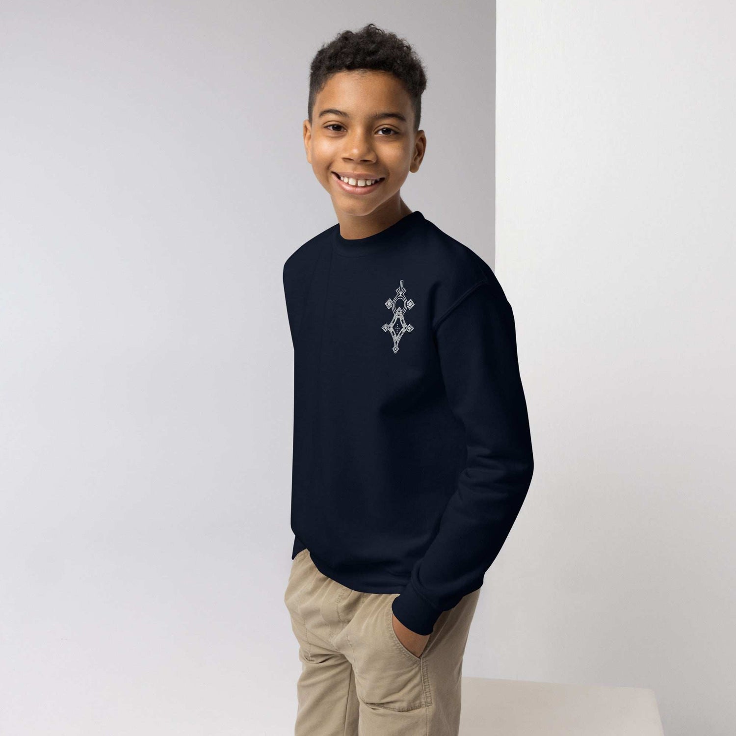 smiling boy wearing navy youth crewneck sweatshirt with geometric design, beige pants, standing indoors